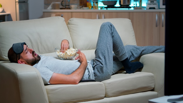 Man liggend in de bank popcron eten en tv kijken