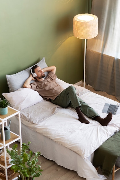 Gratis foto man liggend op bed luisteren naar muziek