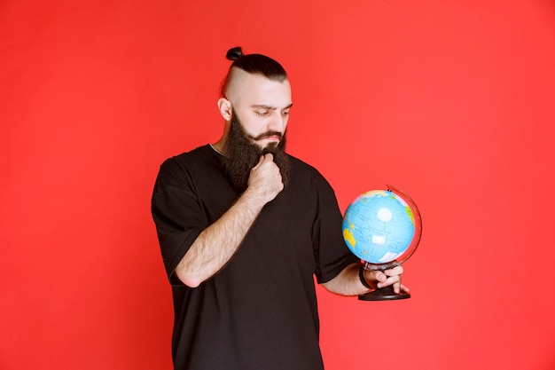 Man met baard die een wereldbol vasthoudt en er plaatsen overheen zoekt.