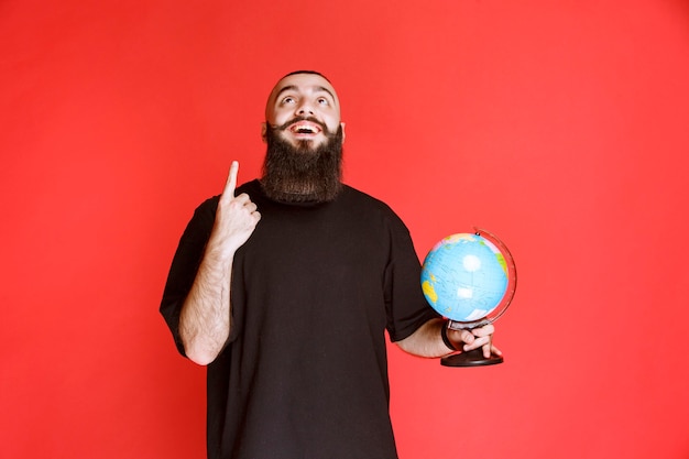 Man met baard die een wereldbol vasthoudt en ergens naar wijst.