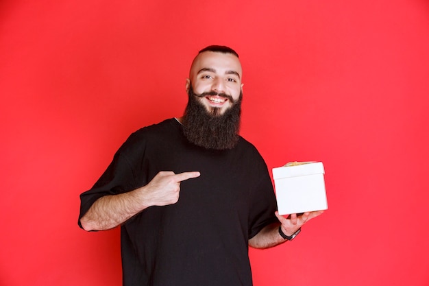 Man met baard die een witte geschenkdoos vasthoudt en ernaar wijst.