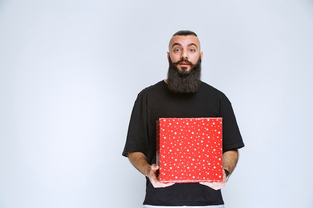 Man met baard die rode geschenkdoos aanbiedt