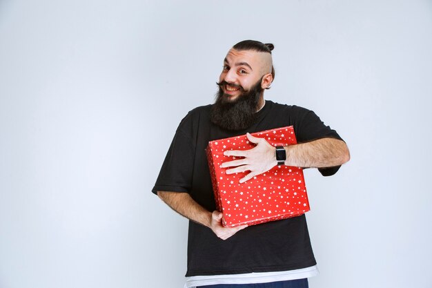 Man met baard die zijn rode geschenkdoos vasthoudt, ervan geniet en zich gelukkig voelt.