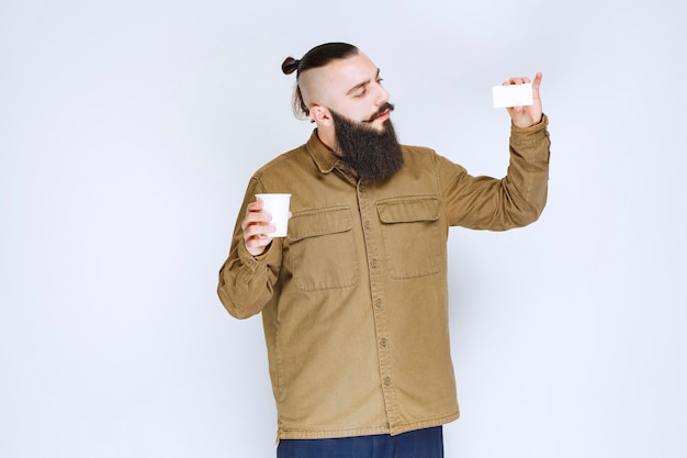 Man met baard die zijn visitekaartje laat zien terwijl hij een kopje koffie vasthoudt.