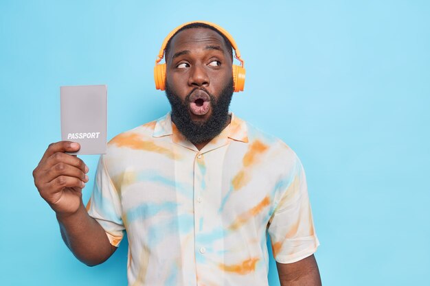man met baard houdt paspoort vast kijkt verrassend weg luistert naar muziek via koptelefoon nonchalant gekleed