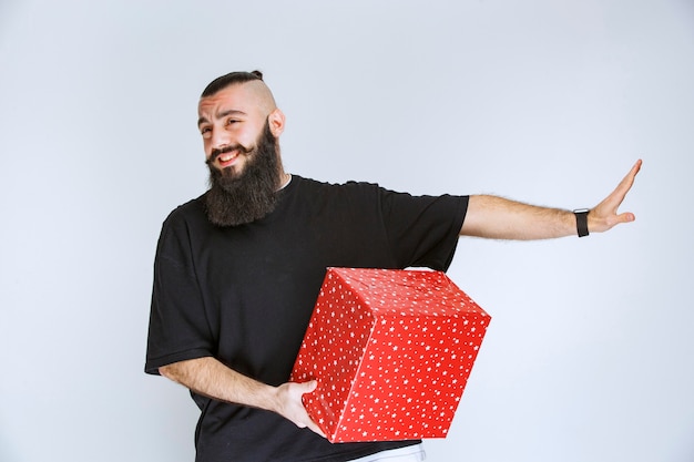 Man met baard met een rode geschenkdoos en kijkt verward en doodsbang.