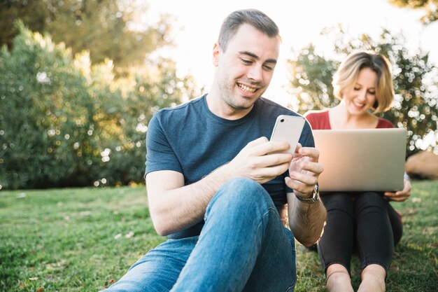 Man met behulp van de smartphone in de buurt van vrouw met laptop