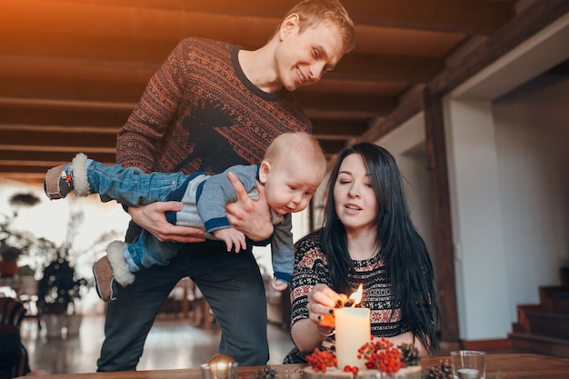 Gratis foto man met een baby in zijn handen te kijken naar zijn vrouw het aansteken van een kaars