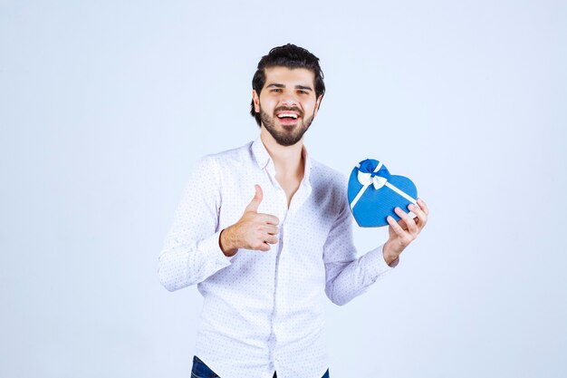 Man met een blauwe geschenkdoos in de vorm van een hart en duim omhoog