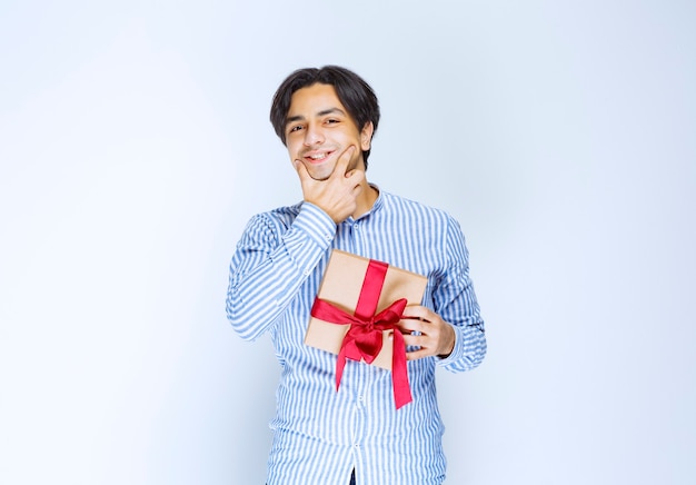 Man met een kartonnen geschenkdoos met rood lint en aarzelend of beschaamd. Hoge kwaliteit foto