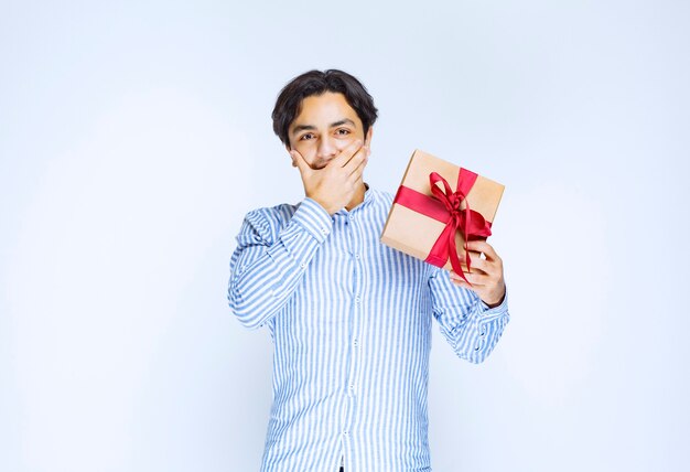 Man met een kartonnen geschenkdoos met rood lint en aarzelend of beschaamd. Hoge kwaliteit foto