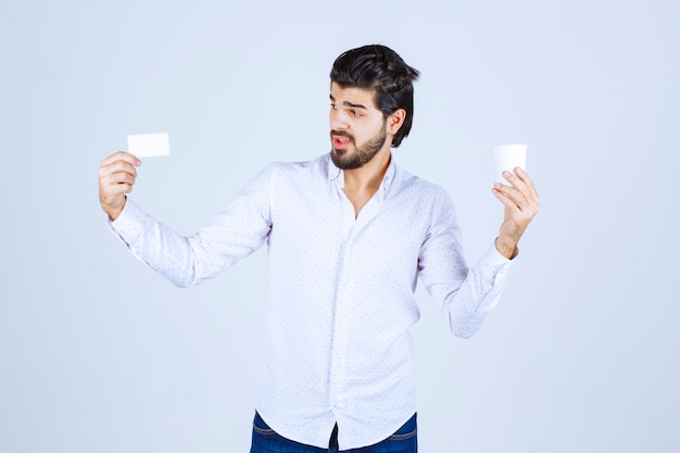 Man met een koffiekopje in de ene hand en zijn visitekaartje in de andere hand