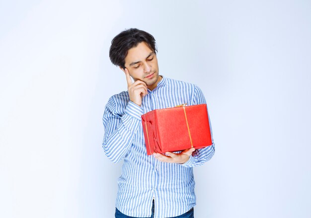 Man met een rode geschenkdoos en ziet er verward en attent uit. Hoge kwaliteit foto