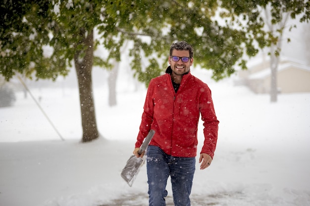 Man met een rode jas en wandelen in een besneeuwd veld terwijl hij de sneeuwschop vasthoudt