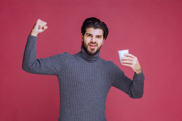 Man met een wegwerp koffiekopje, voelt zich krachtig en energiek.