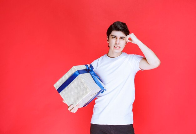 Man met een witte blauwe geschenkdoos en denken