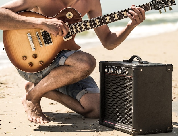 Man met elektrische gitaar op het strand