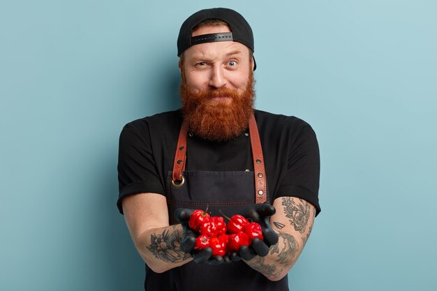 Gratis foto man met gemberbaard die schort en handschoenen draagt die tomaten houden