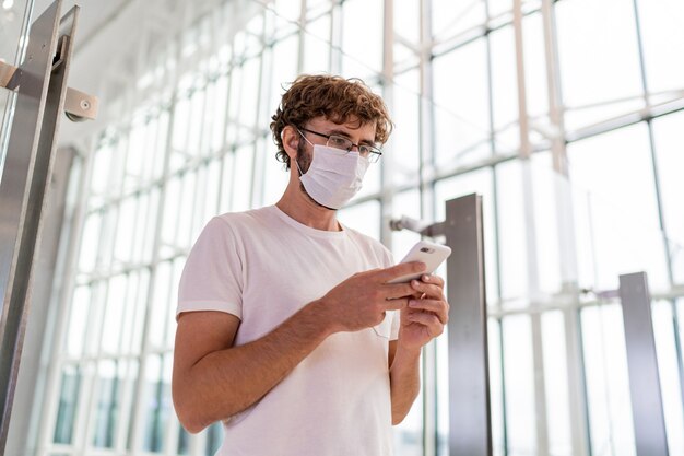 Man met gezichtsmasker in luchthaven en met behulp van smartphone