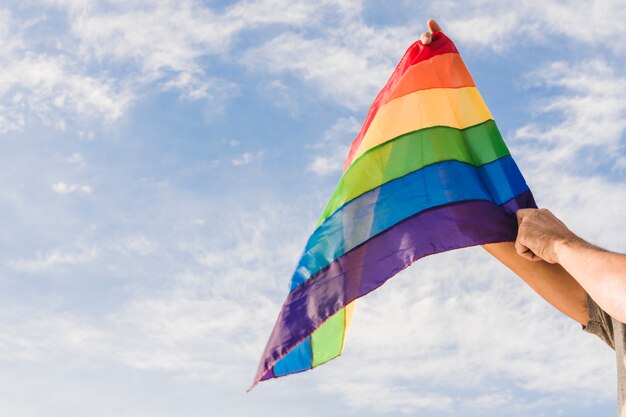 Man met grote vlag in LGBT-kleuren en blauwe hemel