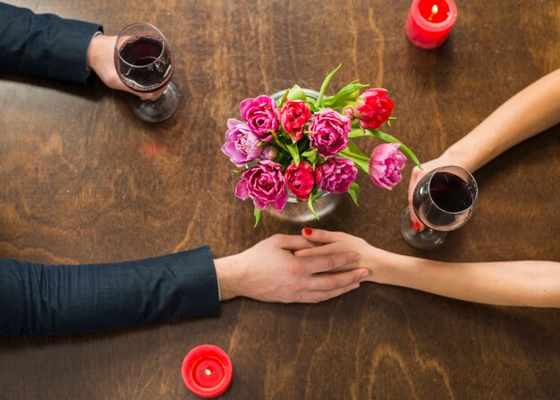 Man met handen met vrouw aan tafel met glazen en bloemen