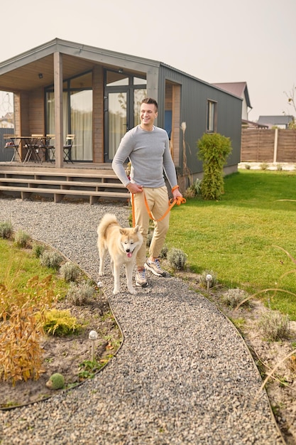 Gratis foto man met hond aan de leiband wandelen in de buurt van landhuis