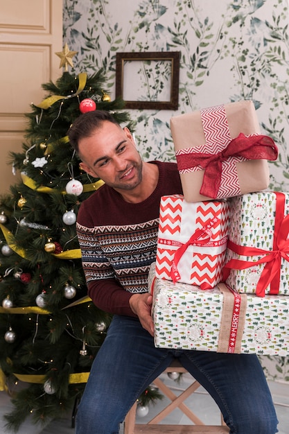 Man met hoop geschenken op stoel in de buurt van de kerstboom