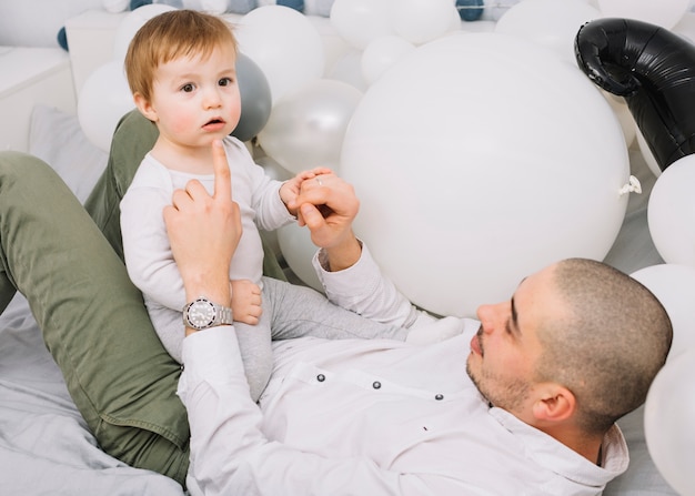 Man met kleine baby spelen op bed in de buurt van ballonnen