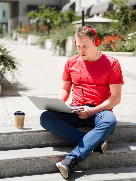 Man met koptelefoon buitenshuis met koffie en laptop