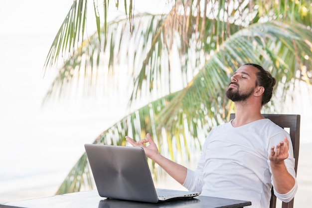 Man met laptop zittend op strand café in de buurt van palmen en yoga
