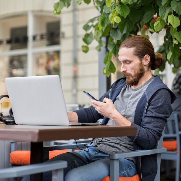 Gratis foto man met smartphone en laptop op stadsterras