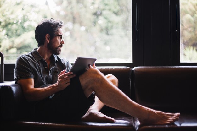 Man met tablet uitkijkend raam