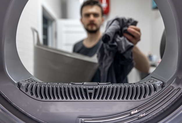 Man met vuile doek in de hand bekijken binnenkant van wasmachine.