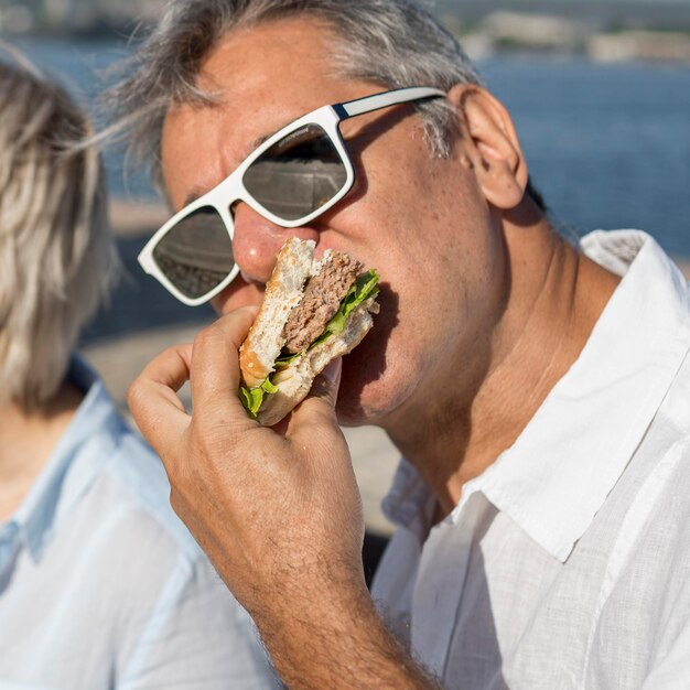 Man met zonnebril buiten eten van een hamburger