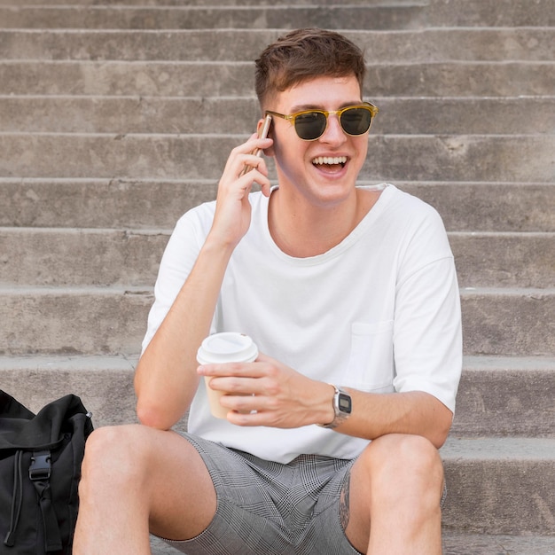 Man met zonnebril buiten koffie hebben en praten aan de telefoon