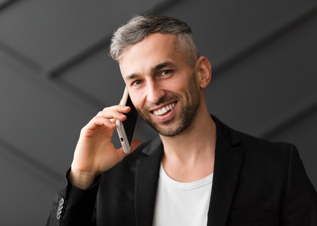 Man met zwarte jas praat over de telefoon en glimlacht