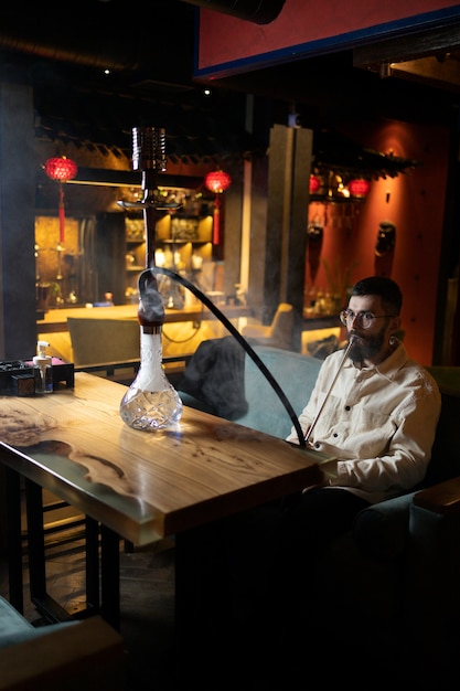 Gratis foto man ontspannen door te vapen van een waterpijp in een bar
