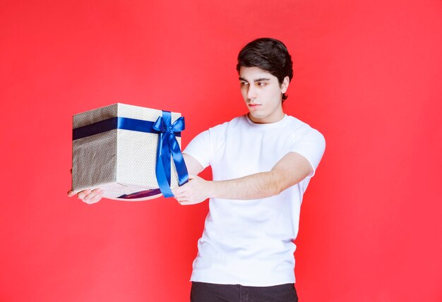 Man ontvangt en houdt een witte geschenkdoos omwikkeld met blauw lint met beide handen