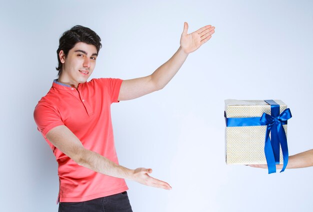 Man ontvangt en houdt een witte geschenkdoos omwikkeld met blauw lint met beide handen