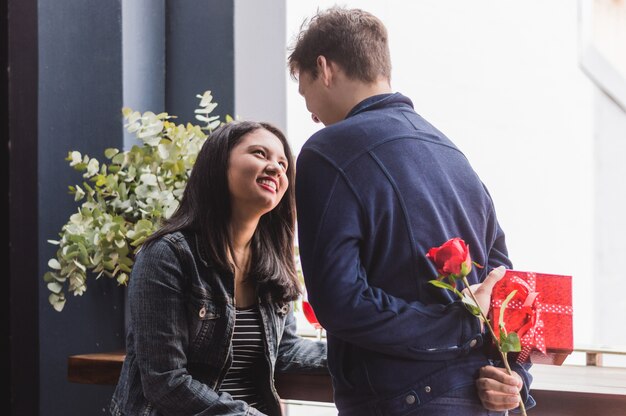 Man praat met zijn vriendin en verbergen op zijn rug een gift en een roos
