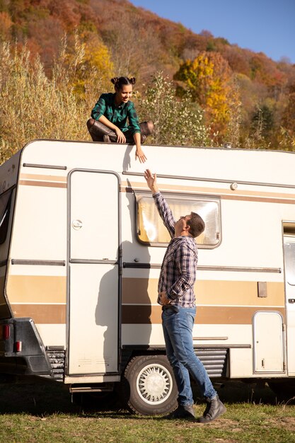 Man probeert zijn vriendin een handje te helpen zittend op het dak van een retro camper. Herfstkleuren