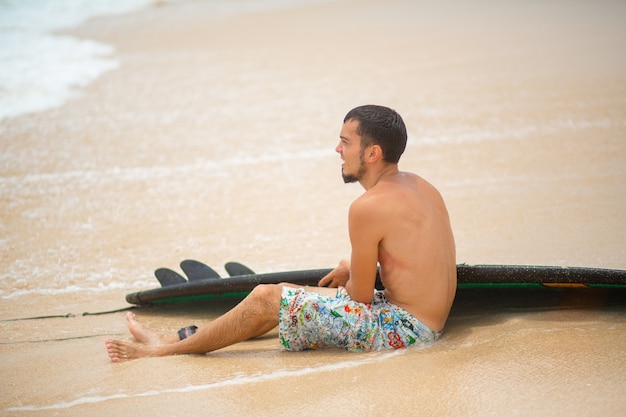 Man rust op tropische zandstrand na het rijden surfen. gezonde actieve levensstijl in de zomer roeping