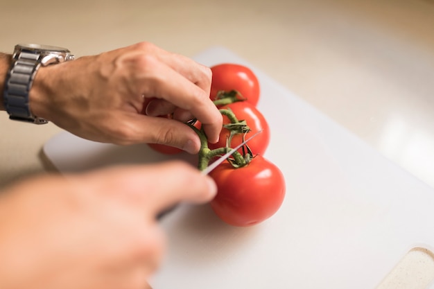 Man&#39;s hand snijden stengel van rode tomaten met een scherp mes