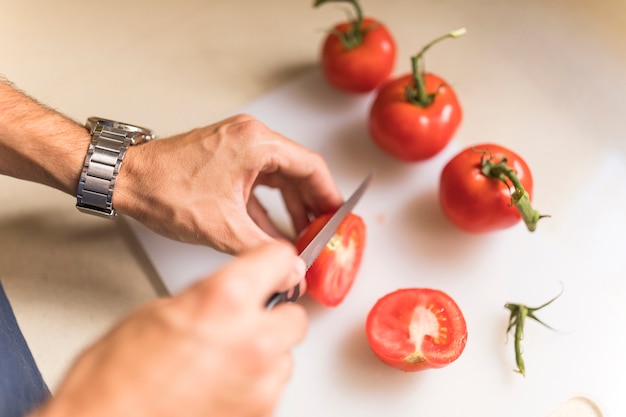 Man&#39;s hand snijden tomaat op snijplank