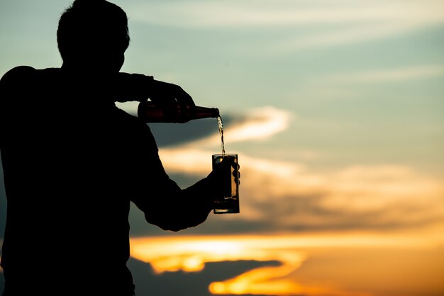 man silhouet met een biertje tijdens een zonsondergang