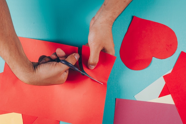 Man snijden vormen van gekleurd papier op cyaan blauw