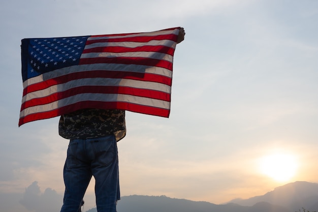 Man staat en houdt de vlag van de VS vast bij zonsopgang