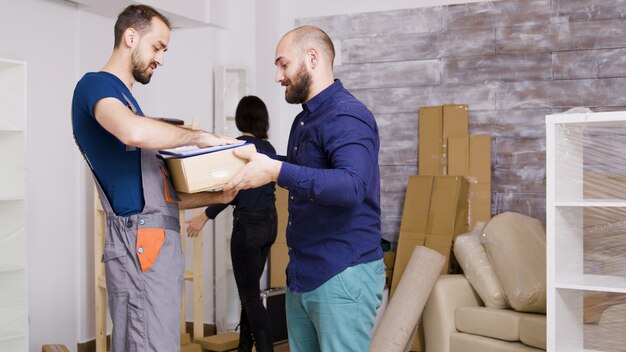 Man van bezorgservice arriveert met dozen en te ondertekenen documenten. Mooie jonge paar verhuizen naar binnen.