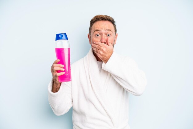 Man van middelbare leeftijd die mond bedekt met handen met een geschokt shampoo fles