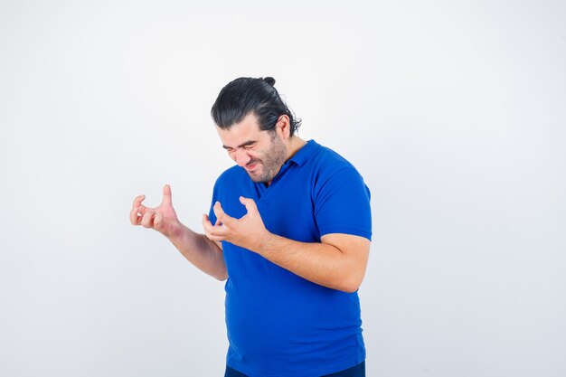 Man van middelbare leeftijd houden handen op agressieve manier in polot-shirt en kijkt boos. vooraanzicht.